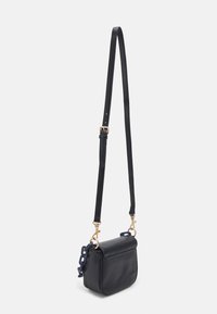 Borsa a tracolla in pelle nera con tracolla regolabile, ganci dorati e dettaglio in catena blu sul lato, sospesa su sfondo bianco.