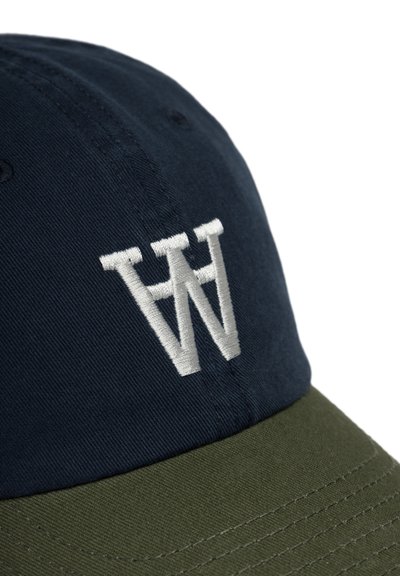 Cappello con corona blu navy e visiera verde oliva. Presenta un logo "W" ricamato in bianco in rilievo. La superficie è liscia, il tessuto è cotone.