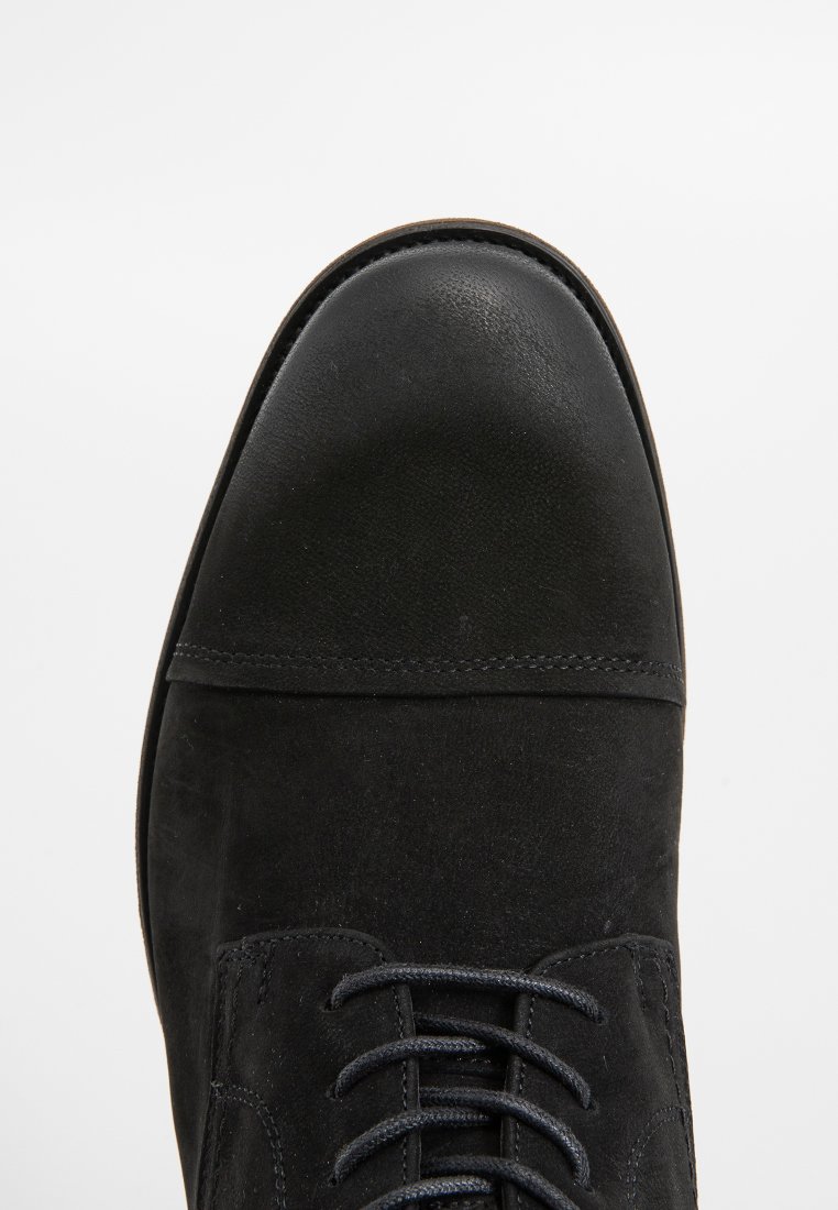 Schwarze Wildlederstiefel mit runder Zehenform, strukturiertem Material, gesteppten Akzenten und Schnürsenkeln vorne. Verfügt über eine glatte Lederkappe auf der Zehe.