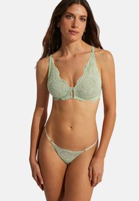 Soutien-gorge en dentelle vert menthe avec des bords festonnés et des motifs circulaires intriqués ; le string en dentelle assorti présente des fines bretelles et des accents de quincaillerie circulaires.