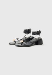 Sandalias de tacón bloque de cuero negro con tiras finas, acentos circulares dorados y detalles de envoltura texturizada en el tobillo.