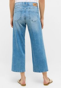 Jean large bleu clair en denim, avec une taille haute, cinq poches et un patch en cuir avec logo sur la ceinture arrière.