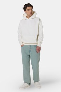 White hooded sweatshirt with front pocket, relaxed fit, paired with light blue jeans and white sneakers, standing on a plain background.