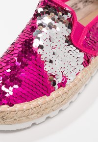 Gros plan d'une chaussure à enfiler rose avec des sequins brillants réversibles roses et argentés et une bordure en jute tissée au-dessus d'une semelle en caoutchouc blanche.