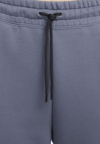 Close-up van grijze sweatpants met een elastische tailleband en een zwarte koord die in een knoop is gebonden.