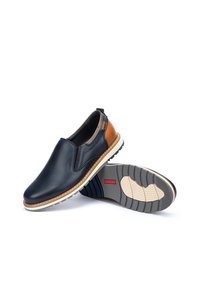 Zapatos slip-on que presentan cuero azul marino con detalles en marrón, una entresuela blanca y una suela de goma texturizada para mejorar el agarre y la flexibilidad.