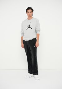Graues Langarmshirt mit schwarzem Jordan-Logo, kombiniert mit schwarzen Velours-Hosen mit Seitenstreifen und weißen Turnschuhen. Minimalistisches Design.