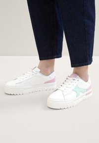 Sneaker bianche con accenti verde menta e rosa, caratterizzate da lati testurizzati, suola voluminosa e dettagli perforati nella zona delle dita.