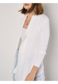 Witte geribde cardigan met een open voorkant, voorzien van lange mouwen en een getextureerde onderrand met kantdetails. Draagt over een nauwsluitend tanktop.