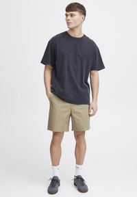 T-shirt en coton gris foncé à manches courtes et col rond, porté avec un short kaki. Le modèle porte des chaussures grises et des chaussettes blanches.