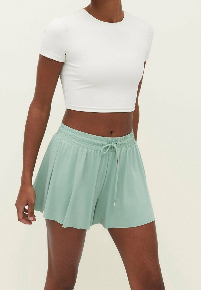 Mintgroene sportkorte broek met een uitlopende pasvorm, elastische tailleband en trekkoord. Gecombineerd met een aansluitend wit cropped T-shirt.