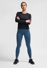 Czarna bluzka z długim rękawem w dopasowanym fasonie, połączona z dopasowanymi legginsami w odcieniu teal. Dopełnieniem stroju są czarne buty sportowe.