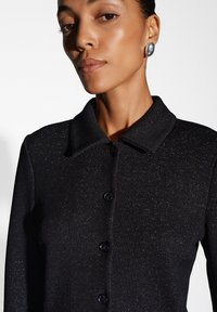 Cardigan nero a coste con colletto, cinque bottoni scuri e sottili accenti di glitter per una texture distintiva.