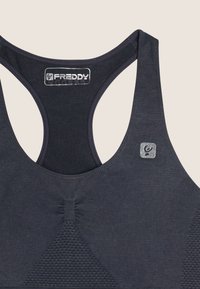 Top sportivo grigio scuro realizzato in un tessuto liscio. Presenta un design a schiena scoperta, pannellature testurizzate e un piccolo logo metallico sul davanti.