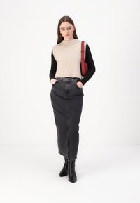 Maglione senza maniche beige a maglia sopra una maglietta nera a maniche lunghe; gonna maxi in denim grigio; stivaletti neri alla caviglia; borsa a spalla rossa.