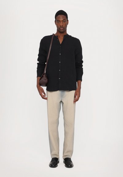 Camicia nera a bottoni con maniche lunghe, jeans grigi chiari e scarpe nere. Una piccola borsa a tracolla marrone pende dalla spalla.