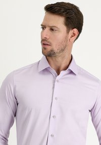 Camicia lungo maniche di colore viola chiaro con colletto classico. Presenta chiusura con bottoni anteriori e texture fine con una leggera lucentezza.