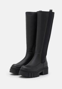 Bottes noires montant jusqu'aux genoux en matériau lisse avec une semelle épaisse, dotées de panneaux élastiques sur les côtés et d'un design robuste.