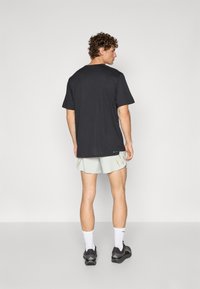 Black short-sleeve t-shirt with a round neckline, paired with light gray shorts featuring yellow accents, worn with dark sneakers and white socks.