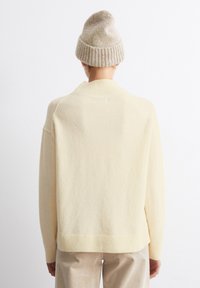 Pulover crem cu guler și tiv cu model, realizat dintr-un material moale. Asortat cu o căciulă tricotată bej și pantaloni de culori deschise.