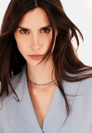 Blusa azzurro chiaro con scollo a V, abbinata a una collana di perline con accenti multicolori e trame varie.