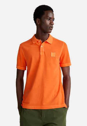 Camisa polo naranja de algodón, con cuello, dos botones y un parche texturizado en el lado izquierdo del pecho. Mangas cortas.