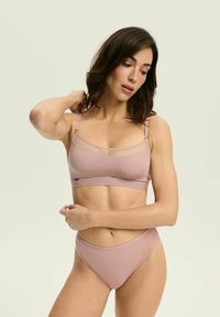 Jasnoróżowy biustonosz braletka z przezroczystymi panelami, regulowanymi ramiączkami oraz pasującymi majtkami typu high-waist z bocznymi wycięciami. Gładka tekstura materiału.