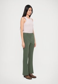 Pantaloni verzi, croiți pe linie dreaptă, asortați cu un top fără mâneci de culoare roz deschis. Material neted și detalii de cusătură minime.