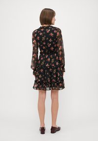 Svart blomstrete kjole med lange, gjennomsiktige ermer, volangkant og elastisk midje. Har flerfargede blomstermønstre over hele.