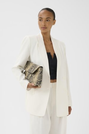 Kvinde iført hvid blazer og bukser over en sort top, der holder en stor clutch med slangeskindsprint.