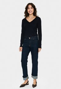 Jūrų laivyno ilgos rankovės V formos iškirptės megztinis derinamas su tamsiai mėlynomis, sulenktomis džinsinėmis kelnėmis. Batai yra tamsūs, su smailiu pirštu. Paprastas, laisvalaikio stiliaus apranga.