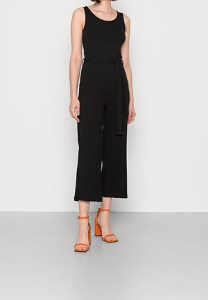 Sort ribbet jumpsuit med brede bukser, knyttet talje og scoop-udskæring, parret med orange remsandaler med blokhæle.