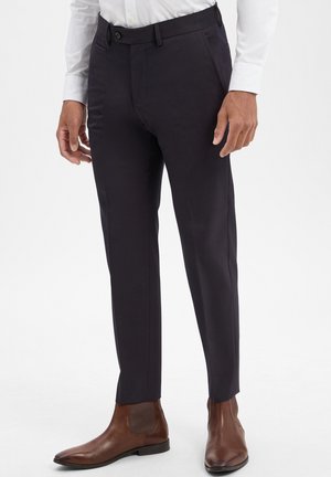 Navy tailored trousers with a smooth texture, flat front, and side pockets, paired with brown leather ankle boots.