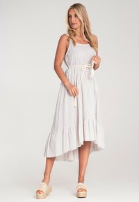 Gestreiftes, ärmelloses Kleid mit tailliertem Bund, gerafftem Saum und asymmetrischem Schnitt. Das Material wirkt leicht und hat eine sanfte Textur.