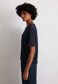 Navyblauwe top met korte mouwen in een ontspannen pasvorm, met een ronde halslijn en een gladde textuur. Gecombineerd met donkere broeken.
