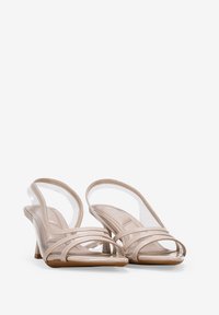 Sandalias de tacón alto, claras y con tiras en un color beige claro, con acentos transparentes y un acabado liso y brillante en las tiras.