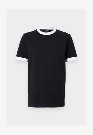 Deux mannequins portant des t-shirts noirs avec des cols blancs et des poignets blancs ; l'un en pantalon large beige, l'autre en short à carreaux longueur genou et une casquette noire.