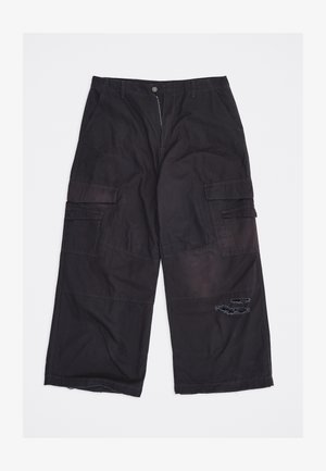 Črne široke cargo hlače z več žepi in poskusno strganino na desnem stegnu, razporejene na ravni beli podlagi.