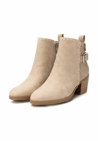 Botas de tobillo beige con acabado de ante suave, puntera de punta, costuras decorativas, cremallera lateral y un acento de cuero perforado detallado.