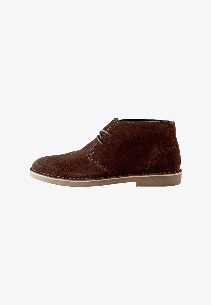 Bottine en suède marron avec un système de laçage, un bout arrondi, des accents de couture et une semelle en caoutchouc léger. Design classique de chukka.
