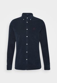 Camicia in velluto a coste blu navy con bottoni bianchi e maniche lunghe, e un piccolo logo ricamato sul petto. Tessuto testurizzato.