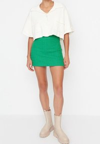 Chemise blanche raccourcie avec poches, mini jupe texturée verte et bottines beiges à semelles épaisses. Tenue décontractée et ajustée.