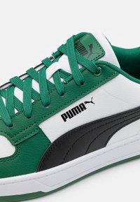 Grønne og hvide sneakers med sorte detaljer, struktureret læderoverdel, hvid sål og grønne snørebånd. Har et sort Puma-logo på siden.