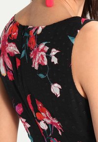 Musta mekko, jossa on vaaleanpunaisia ja punaisia kukkakuoseja, mukana teksturoitu kangas, tiukka muotoilu ja olkaimeton leikkaus. Koristeltu takasaumalla.