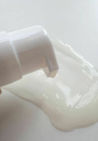 Biała plastikowa pompka dozująca częściowo otwarta, wydobywająca gładki, przezroczysty krem przypominający żel na białą powierzchnię.