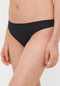 Zwart bikini broekje met een gestructureerd ruitpatroon, gemiddelde bedekking en een zachte elastische tailleband. Naadloos ontwerp bevordert het comfort.