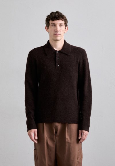 Pull en tricot marron foncé avec un col et une patte de boutonnage à cinq boutons, doté de manches longues et d'une texture douce et duveteuse. Porté sur un pantalon marron.