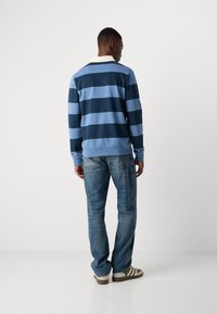 Polo à manches longues rayé bleu et bleu clair avec un col blanc, associé à un jean bleu délavé et des sneakers à lacets noir.