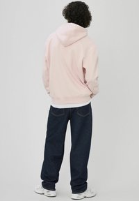 Sweat à capuche rose clair avec une poche kangourou, des poignets et un ourlet côtelés ; associé à un jean en denim bleu foncé. Coupe décontractée et texture lisse.