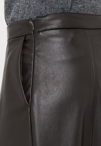 Gonna nera in pelle con una superficie liscia, vita strutturata e tasche laterali discrete. Il capo presenta un design elegante e moderno.